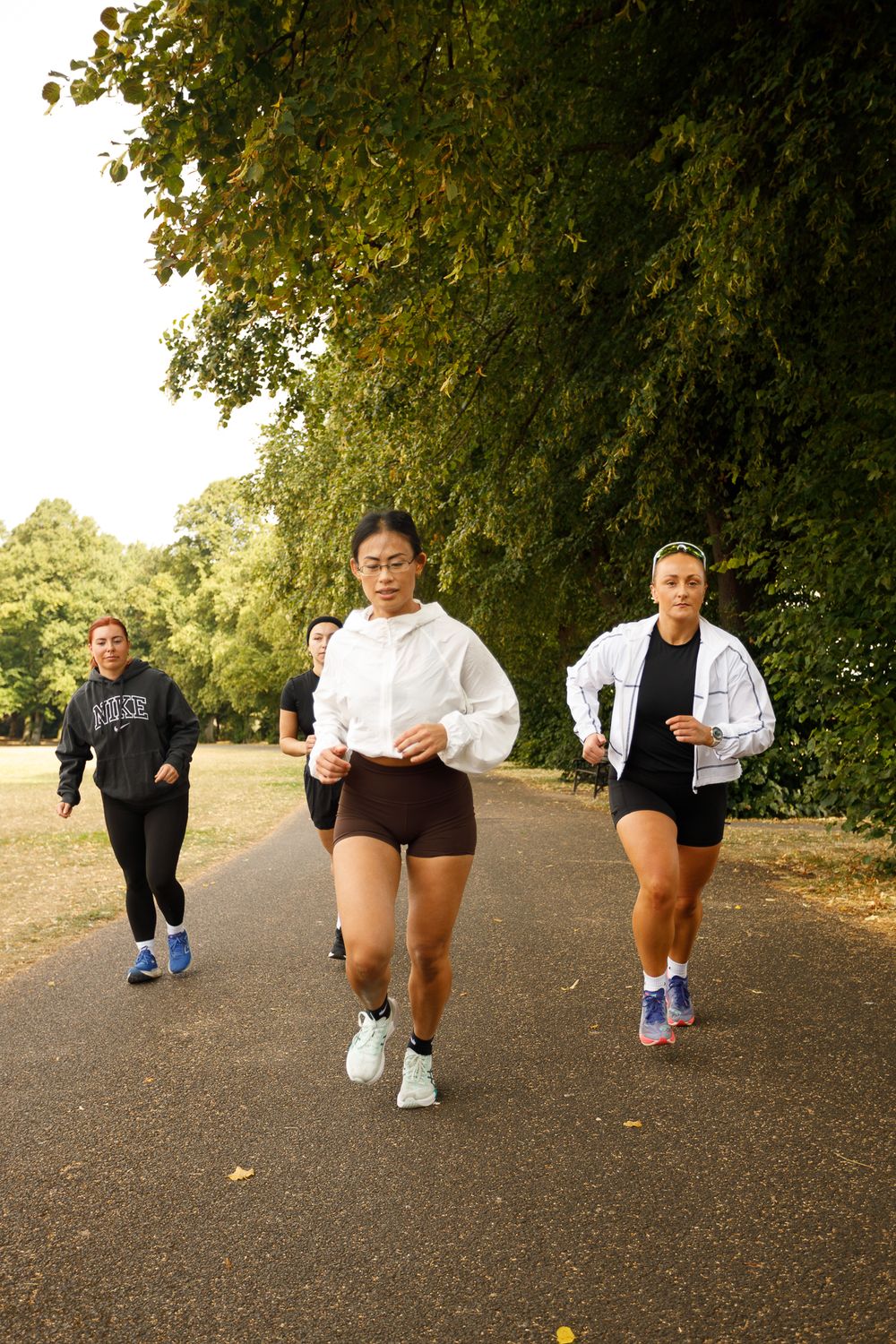 Group of runners jogging together on a tree-lined path during outdoor fitness training session.
