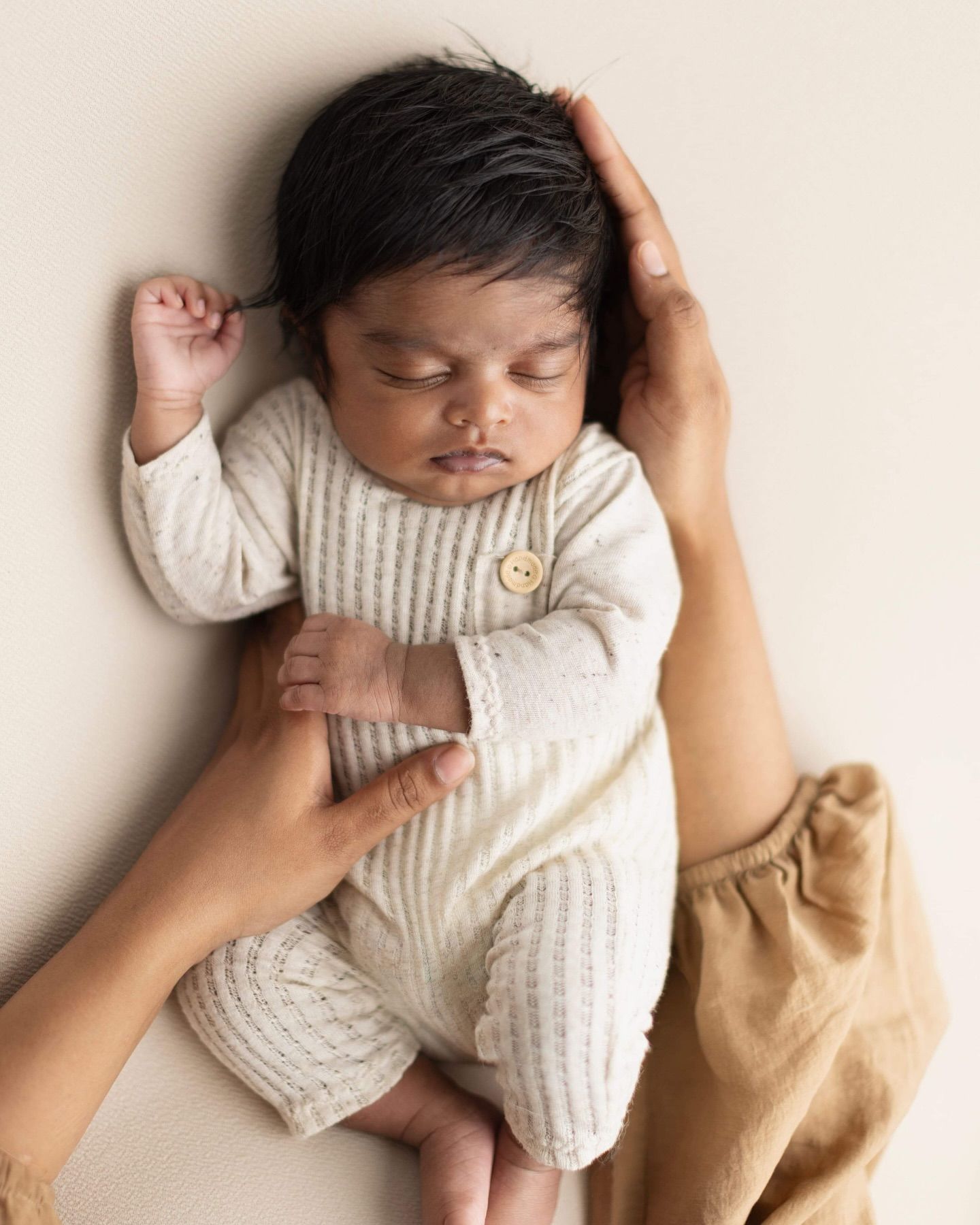 Sleeping newborn baby in white knit outfit lying on cream backdrop in professional studio setting.