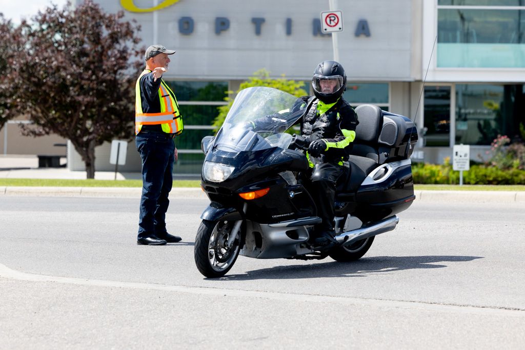 A motorcycle rider in protective gear makes a turn on a black sport bike near a commercial building.