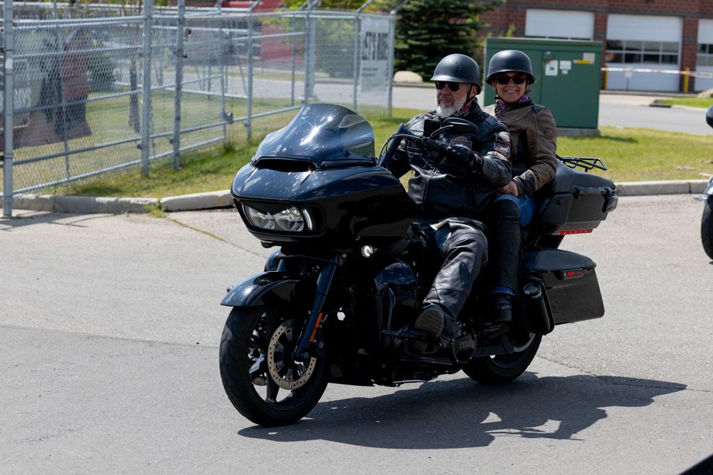 Four black motorcycles parked in a row on a sunny day with riders in dark clothing.