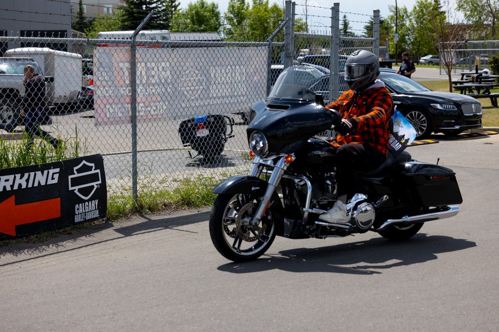 Black Harley-Davidson motorcycle parked on a sunny day with chain link fence in the background.