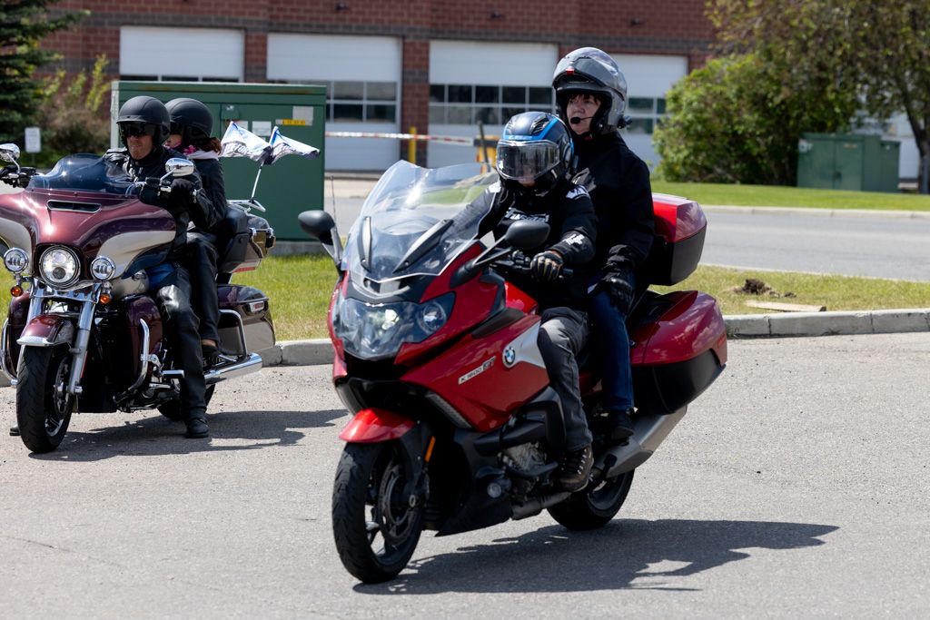 A line of motorcycles parked in a parking lot with riders gathered around on a sunny day.