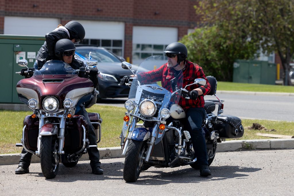 Row of parked motorcycles lined up outside a brick building on a sunny day.