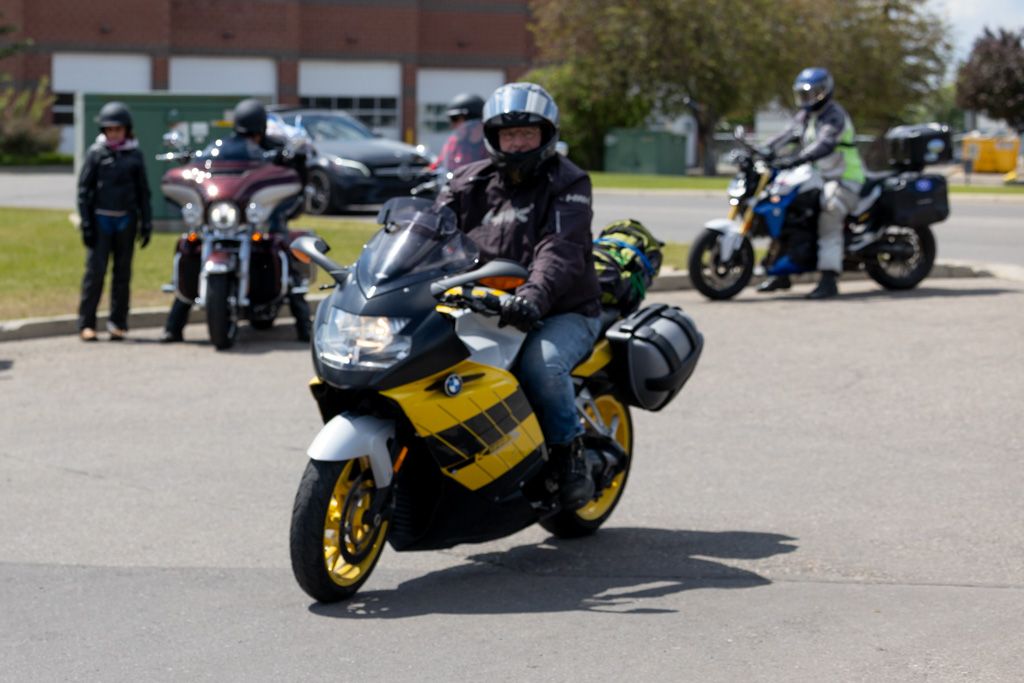 A row of yellow and black motorcycles parked in a parking lot with riders nearby.