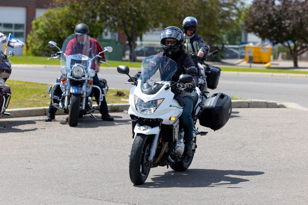 Line of motorcycles parked in a row on sunny day with trees and buildings in background.