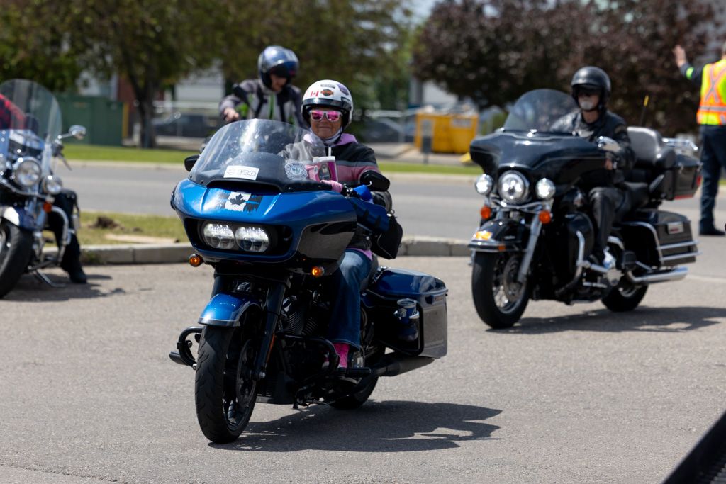 Motorcycles lined up in parking lot with riders in protective gear preparing for group ride.