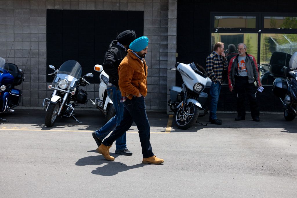 Person in orange hoodie walks past parked motorcycles on a street near a building entrance.