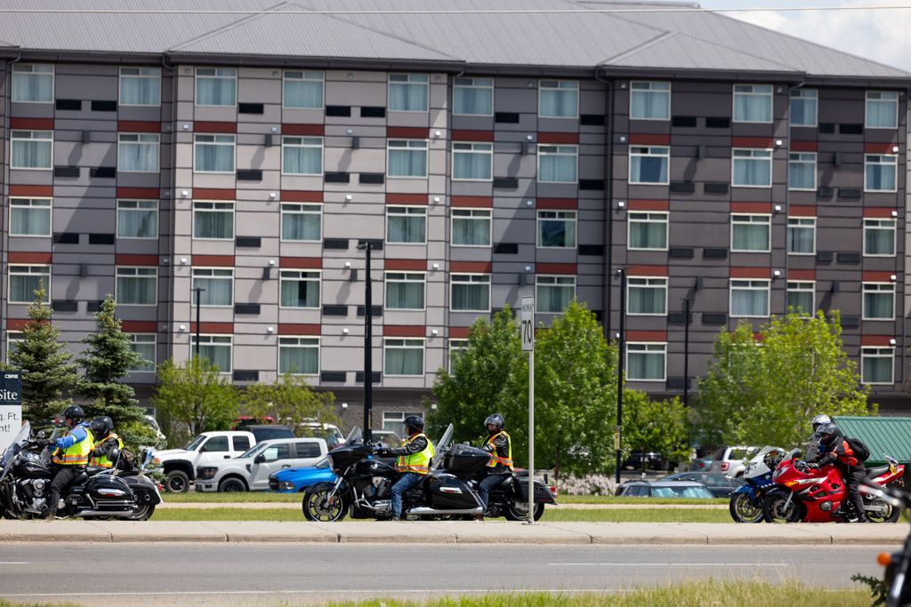 Motorcycles parked outside a modern apartment complex with gray and red facade on a sunny day.