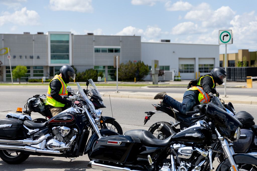 A row of parked motorcycles lined up outside a commercial building on a sunny day.
