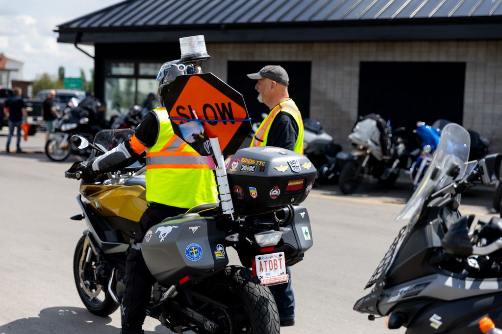 Rows of parked motorcycles lined up at an outdoor event or gathering with a black metal roof visible above.