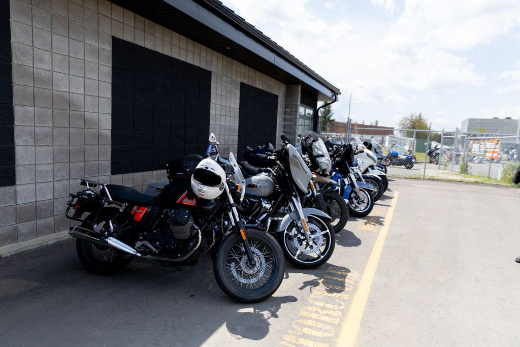 A row of motorcycles parked in a line against a building wall on a sunny day.