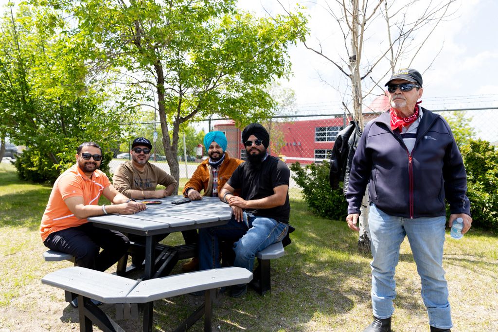 Group of motorcycle enthusiasts gathered outdoors around a table during a community event.