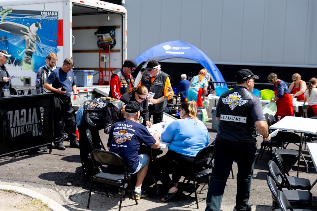 Racing pit crew members work on a motorcycle during a motorsport event under a blue tent at an outdoor venue.