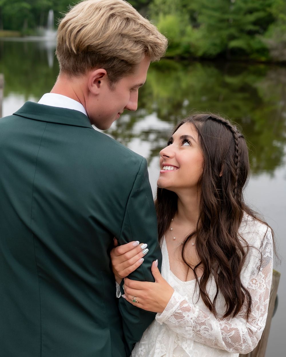 A romantic moment between a couple in wedding attire embracing outdoors with greenery in the background.