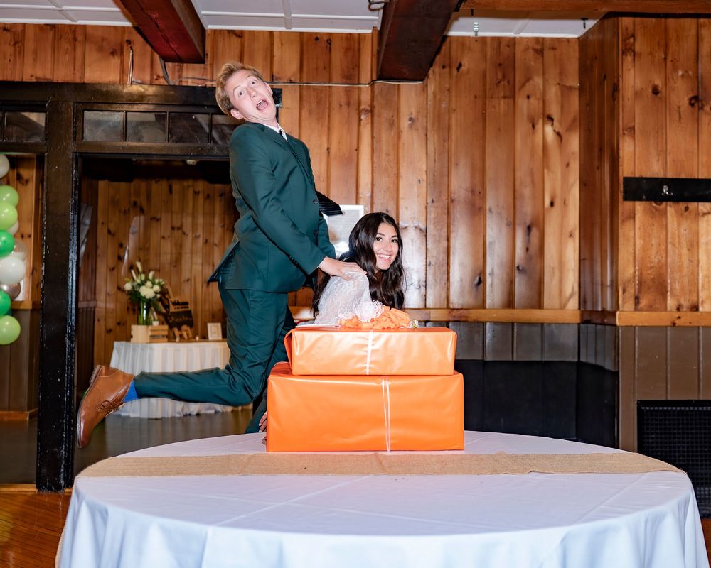 A wedding cake with orange and white tiers is being cut on a table in a rustic wooden venue.