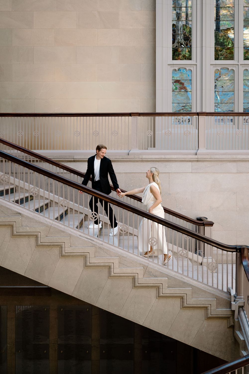 A couple shares a romantic moment on an elegant white marble staircase in a grand building.