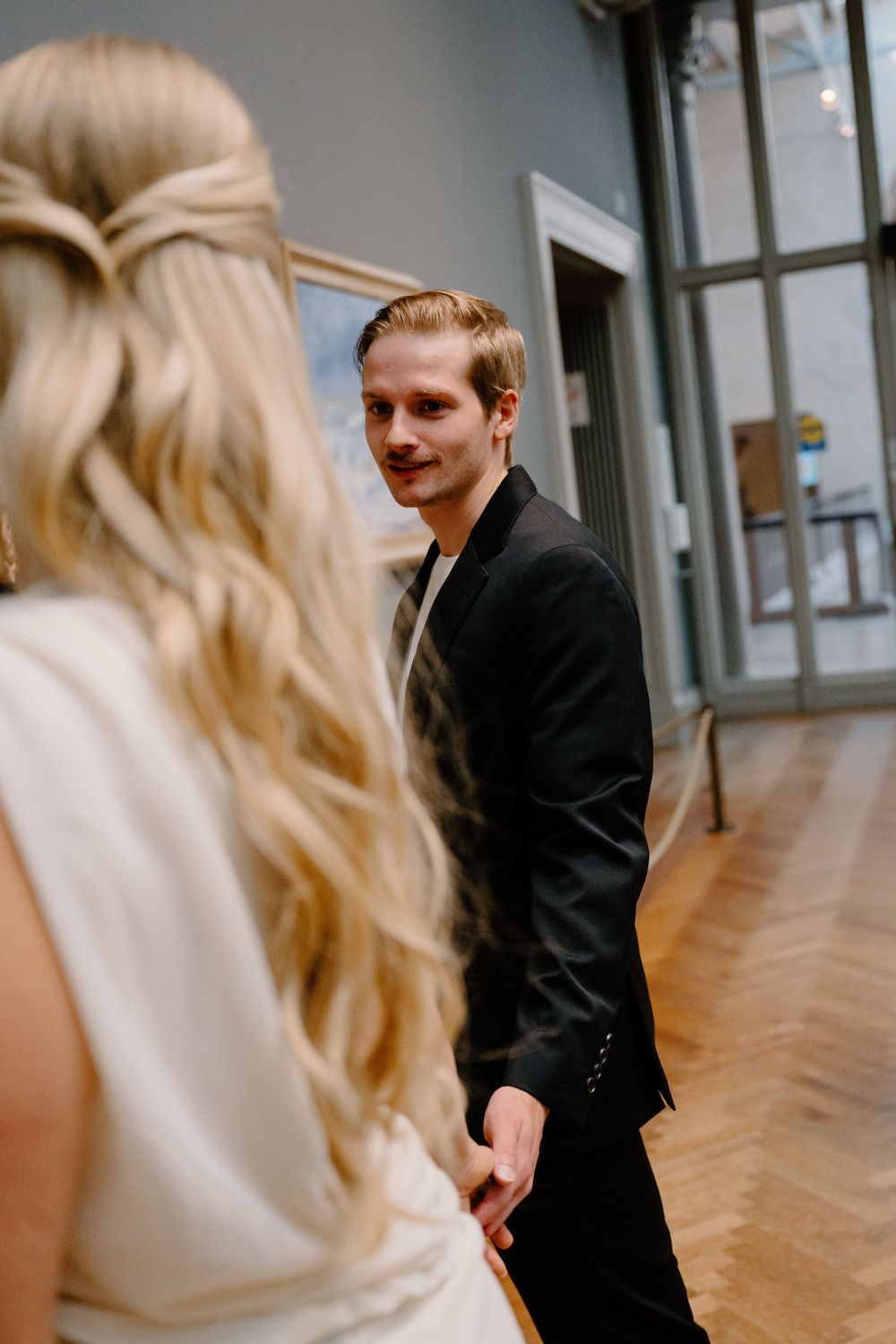 A couple shares a candid moment in a bright hallway with large windows.