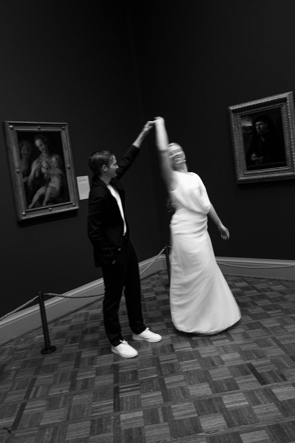 Black and white wedding photos showing playful moments in a dark art gallery setting.