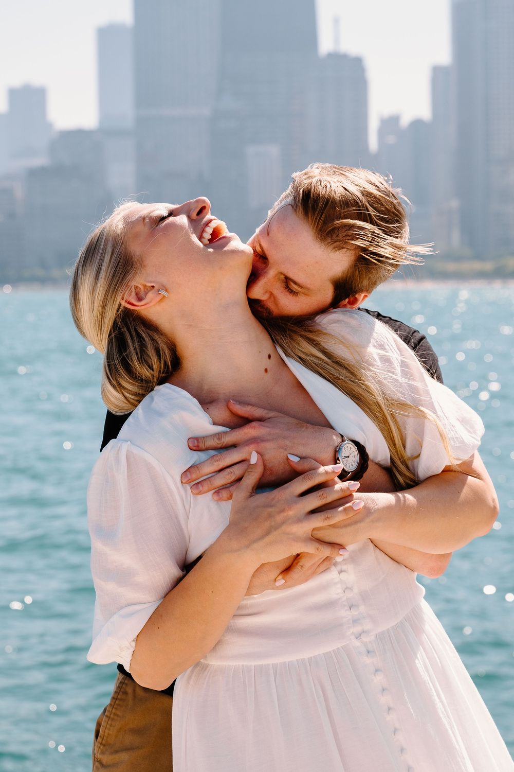 Romantic couple embracing against Chicago skyline backdrop with Lake Michigan sparkling in sunlight.