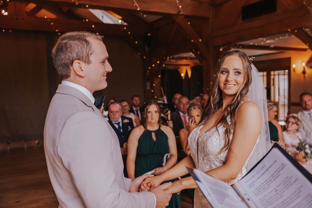 A couple exchanges vows during an indoor wedding ceremony with guests watching in a warmly lit venue.