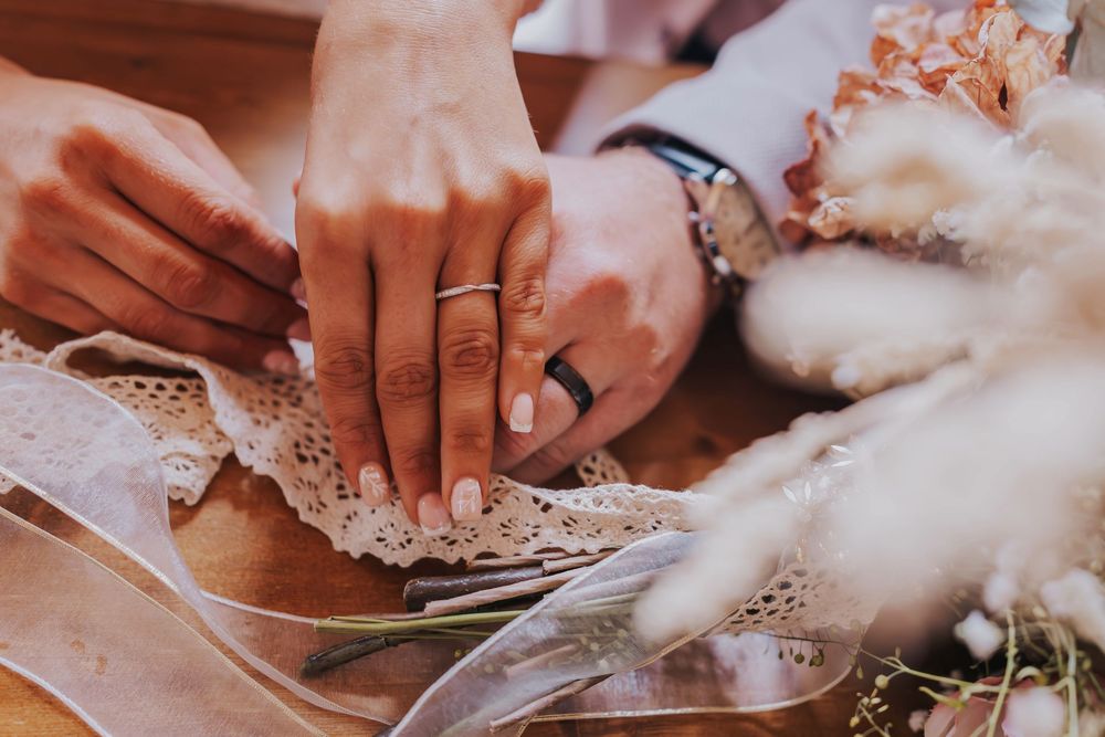 Close-up view of hands holding delicate lace fabric with white cotton flowers and wedding details.
