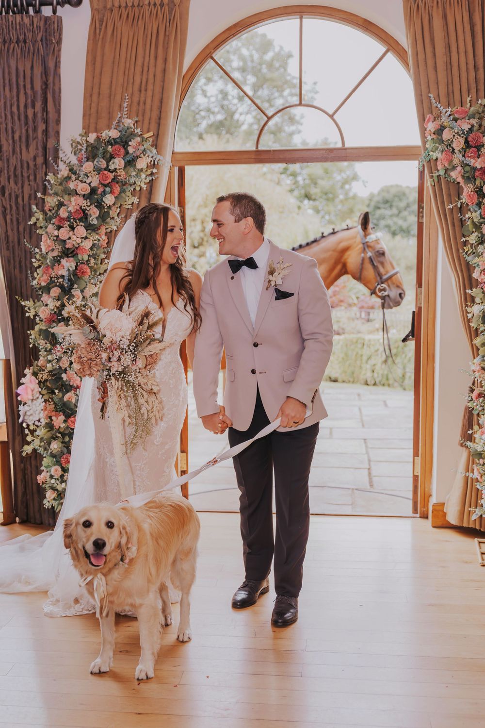 Wedding ceremony in a sunlit room with floral arrangements and a golden retriever participating in the celebration.