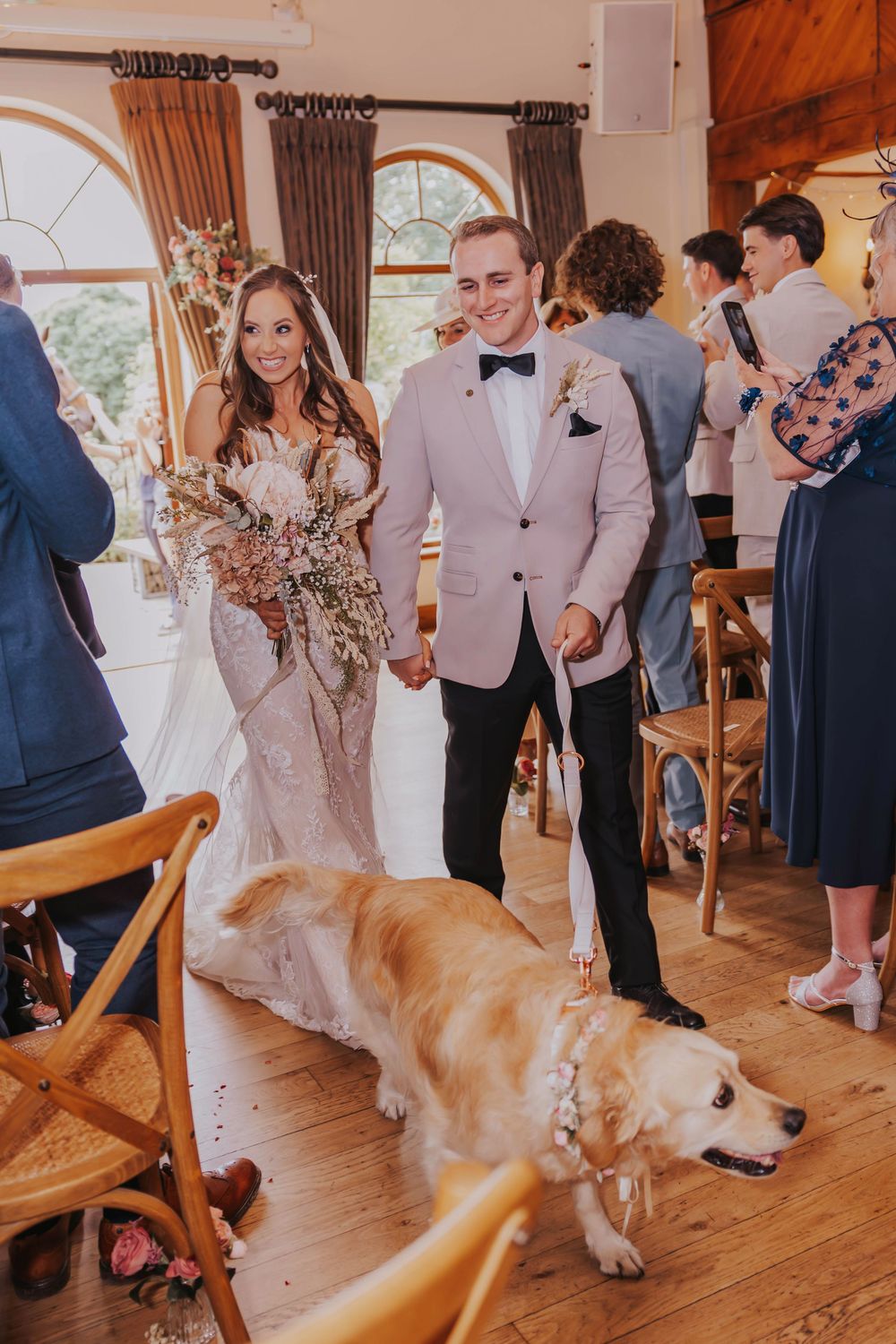A couple celebrates at their wedding reception in a rustic venue with a golden retriever walking past in the foreground.