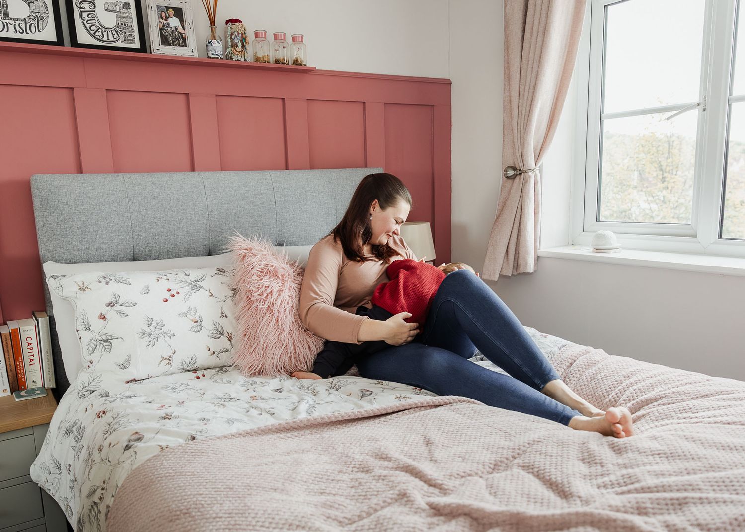 A mum sits on her bed at home and breastfeeds her toddler. She smiles at her son and looks relaxed. Natural Bristol baby photographer