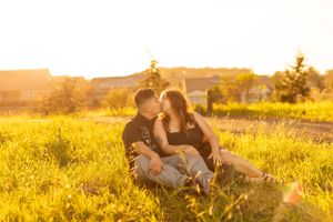 Couple sits in golden sunlit field during warm sunset.