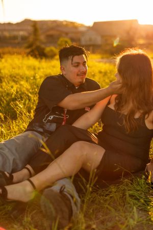 Couple relaxing together in grass field during sunset golden hour.