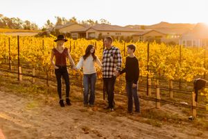 Four people stand together in a vineyard at sunset with golden lighting.