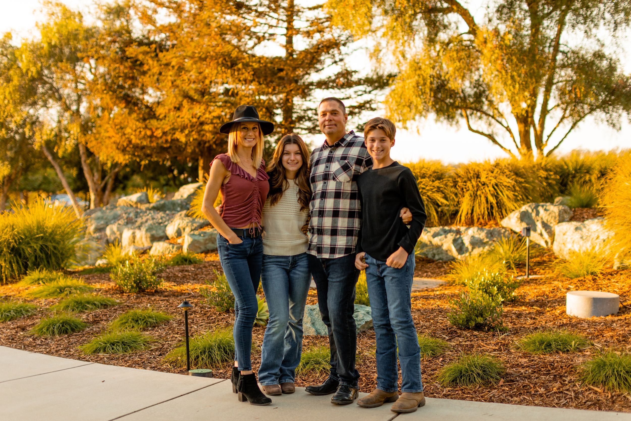 Group poses together outdoors during golden hour with fall foliage in background.