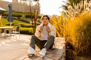 Person in casual attire sits on concrete ledge during golden hour.