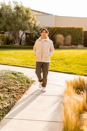 Person in light jacket walks on sidewalk during golden hour.