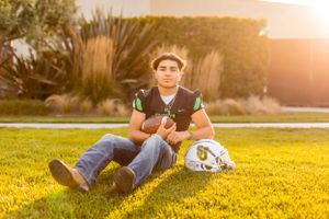 Football player sits on grass field with equipment during sunset.