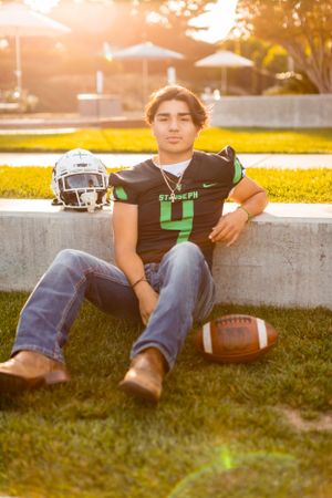 Football player in jersey poses with equipment during golden hour.