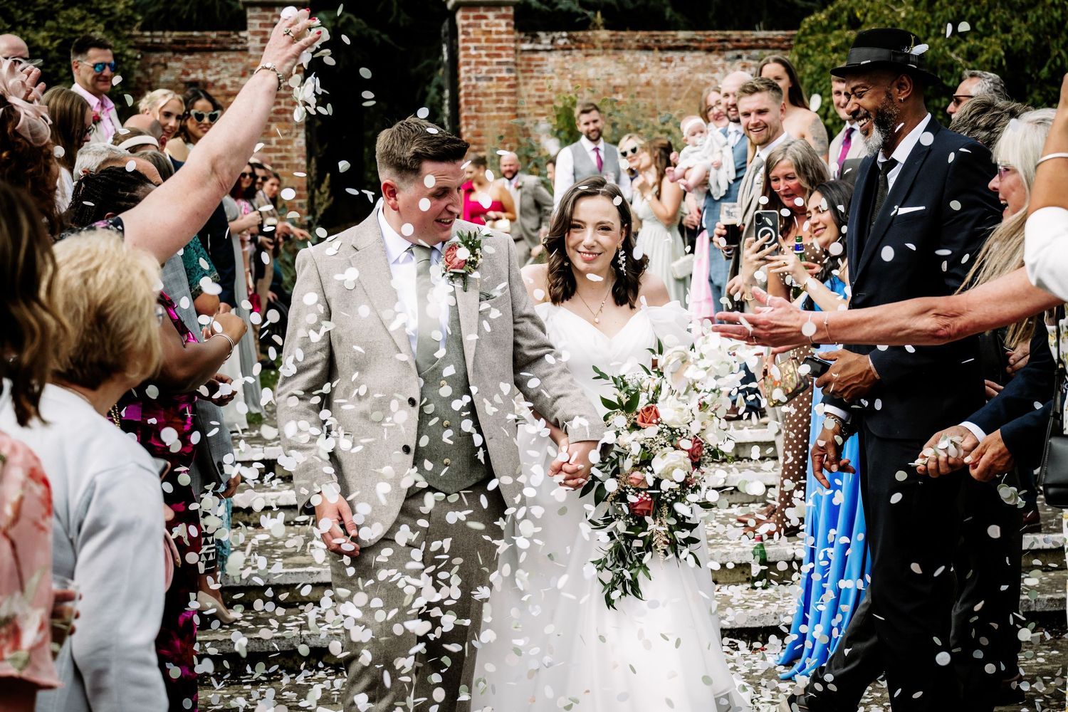 Wedding guests throwing white confetti during outdoor celebration.