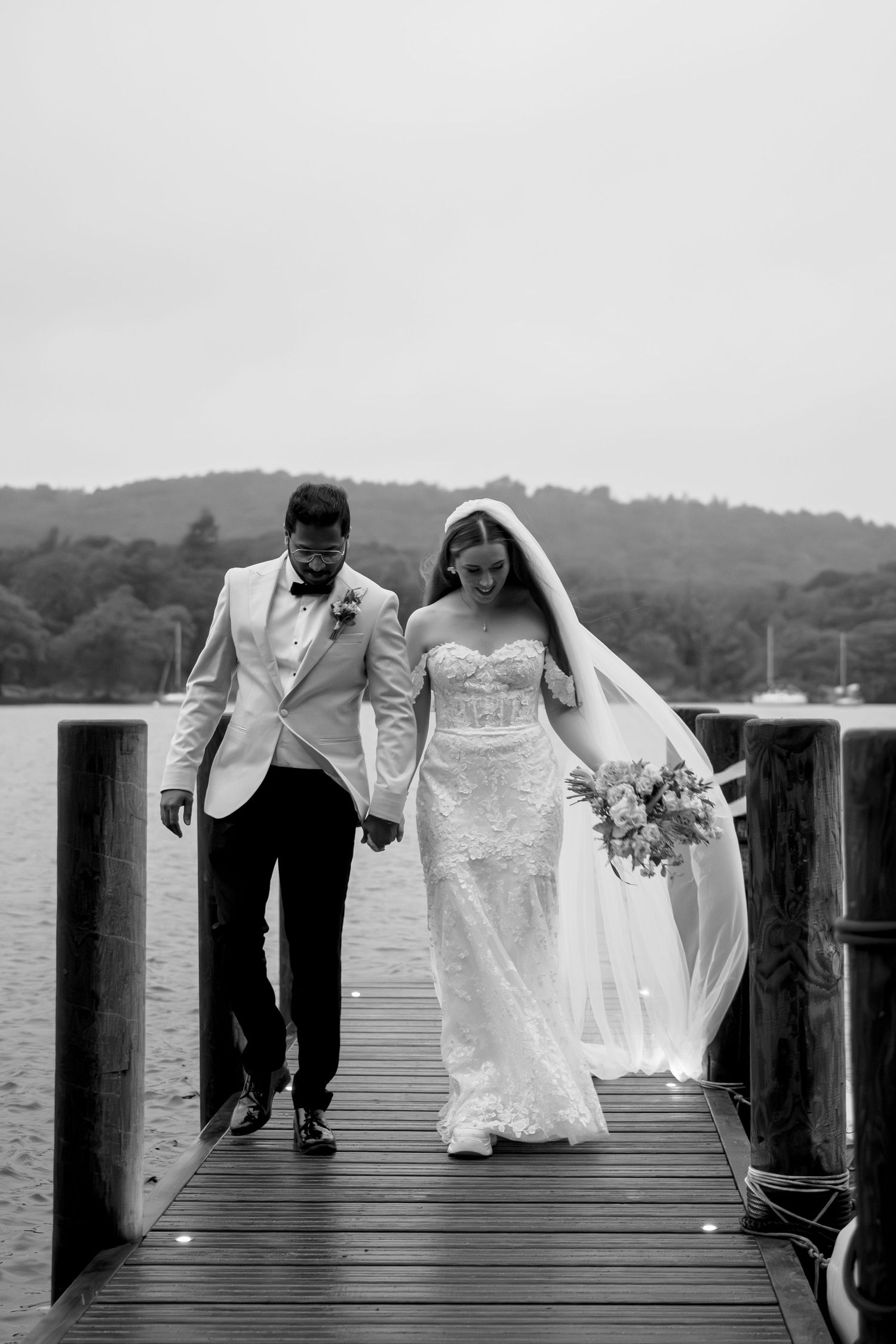 Wedding couple walking together on a wooden dock by a lake in black and white.