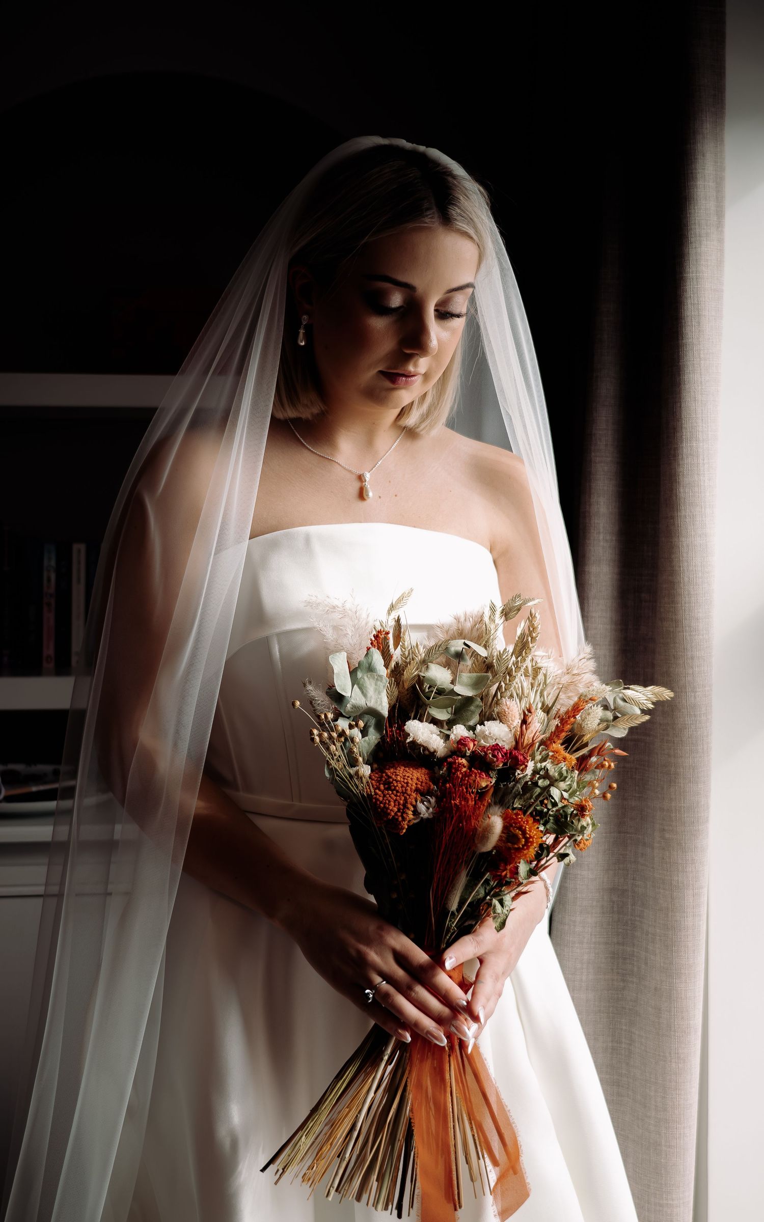 Artistic bridal portrait with dramatic lighting and a dried flower bouquet.
