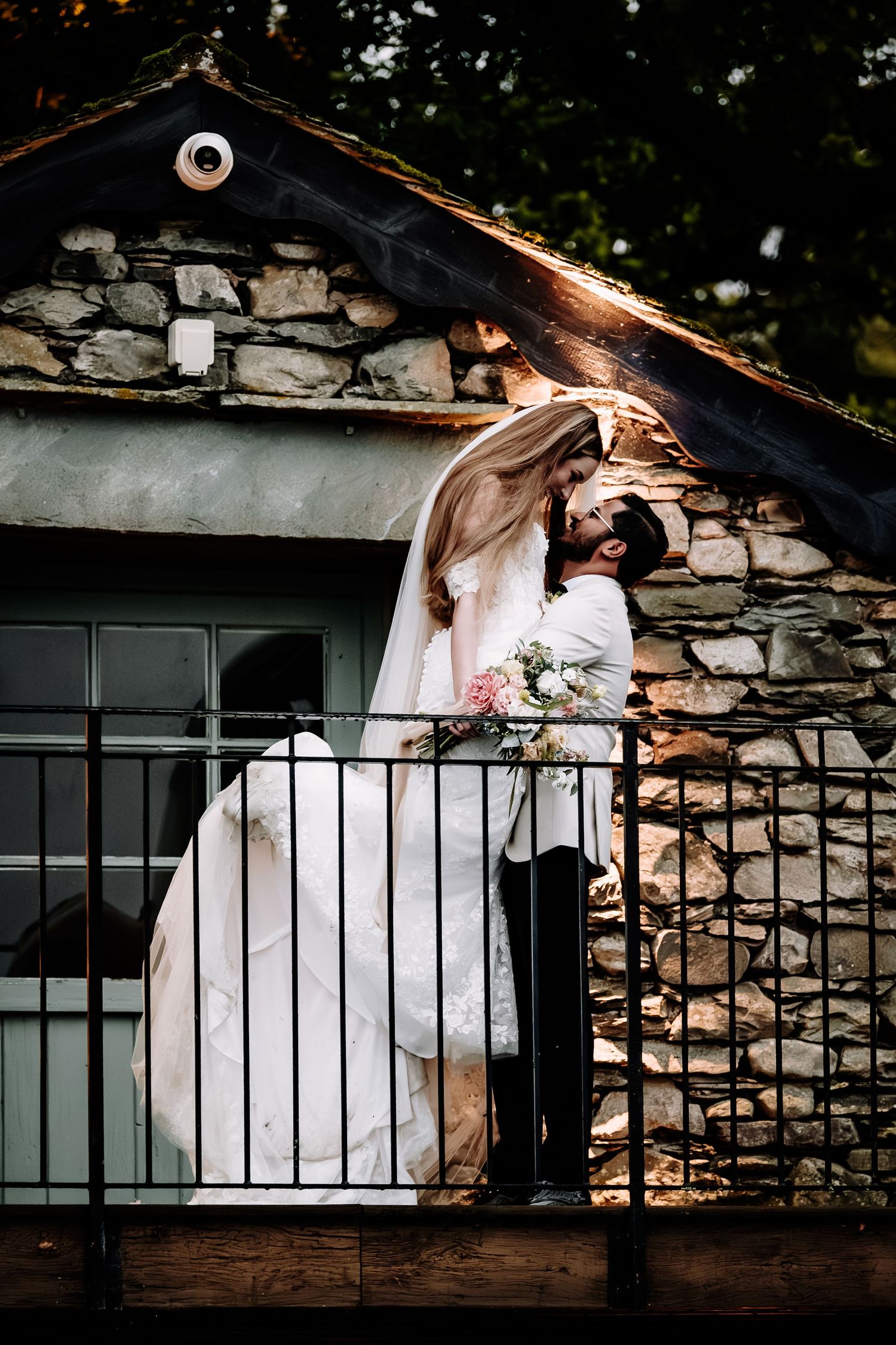 Artistic wedding portraits against a rustic stone wall with metal railing.