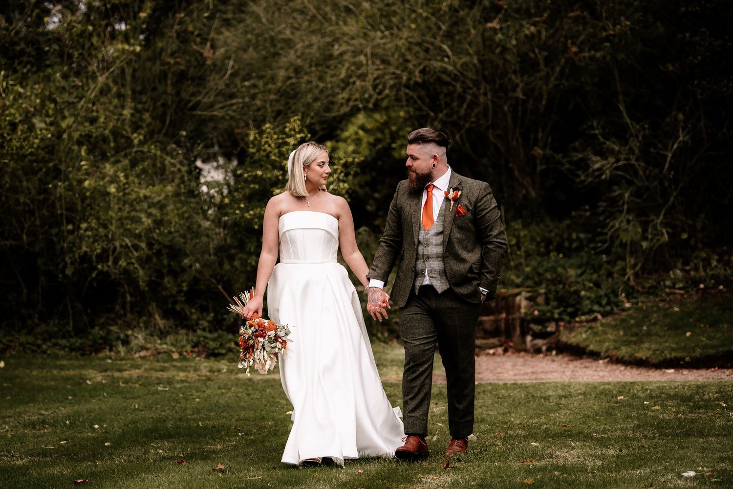 Bride and groom walking hand in hand through a lush garden setting.