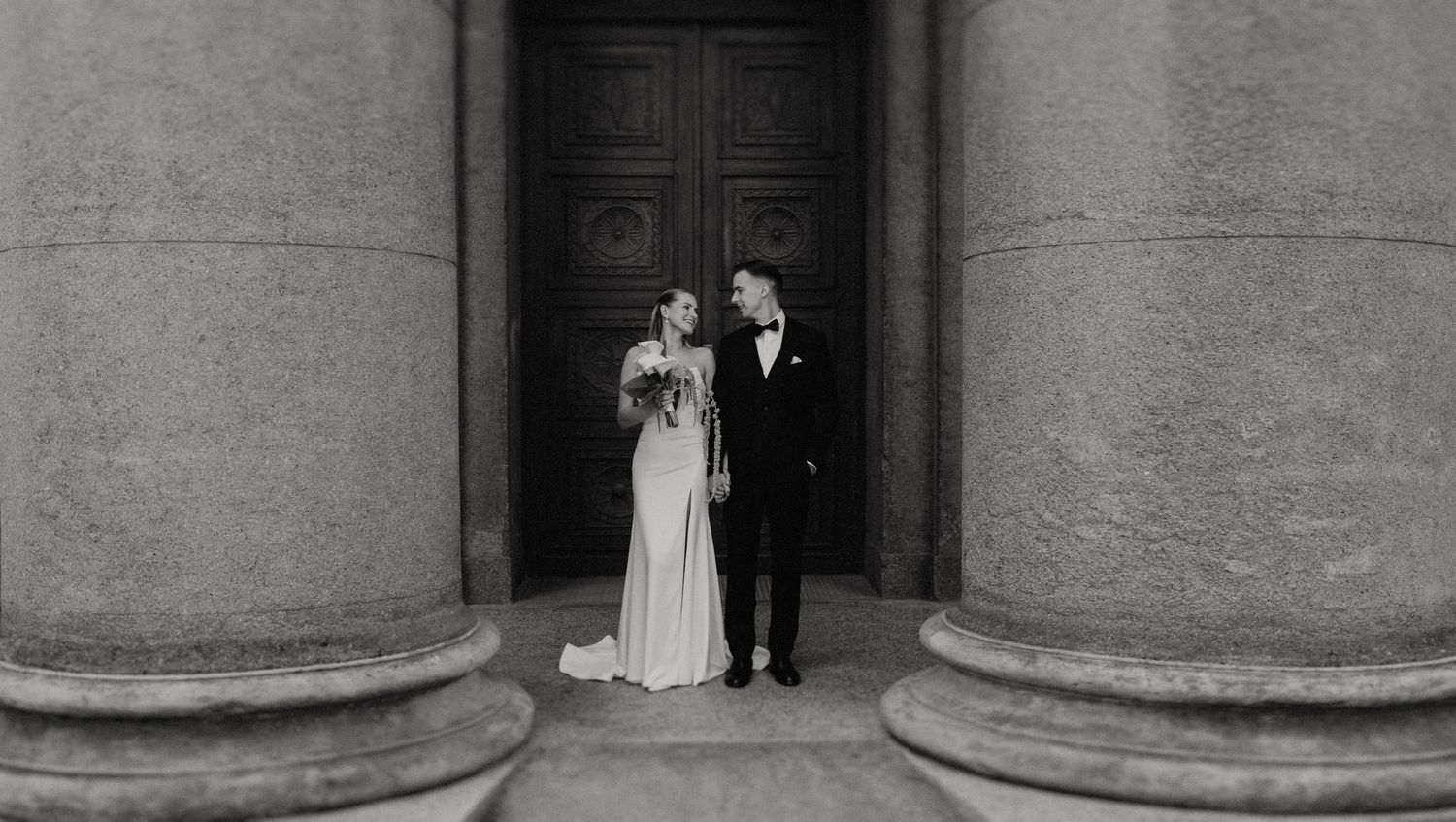 Stone colonnade with ornate doors provides elegant backdrop for wedding photography.
