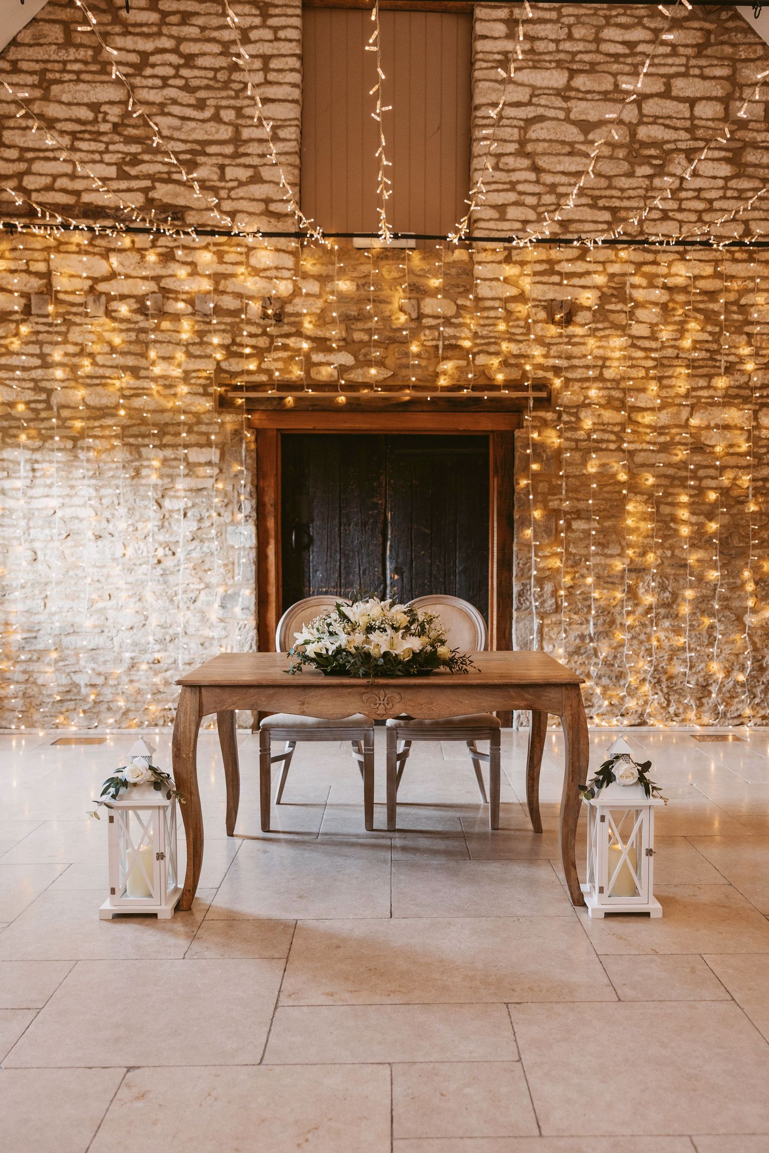 Rustic stone wall venue decorated with hanging string lights and elegant table settings for a wedding reception.