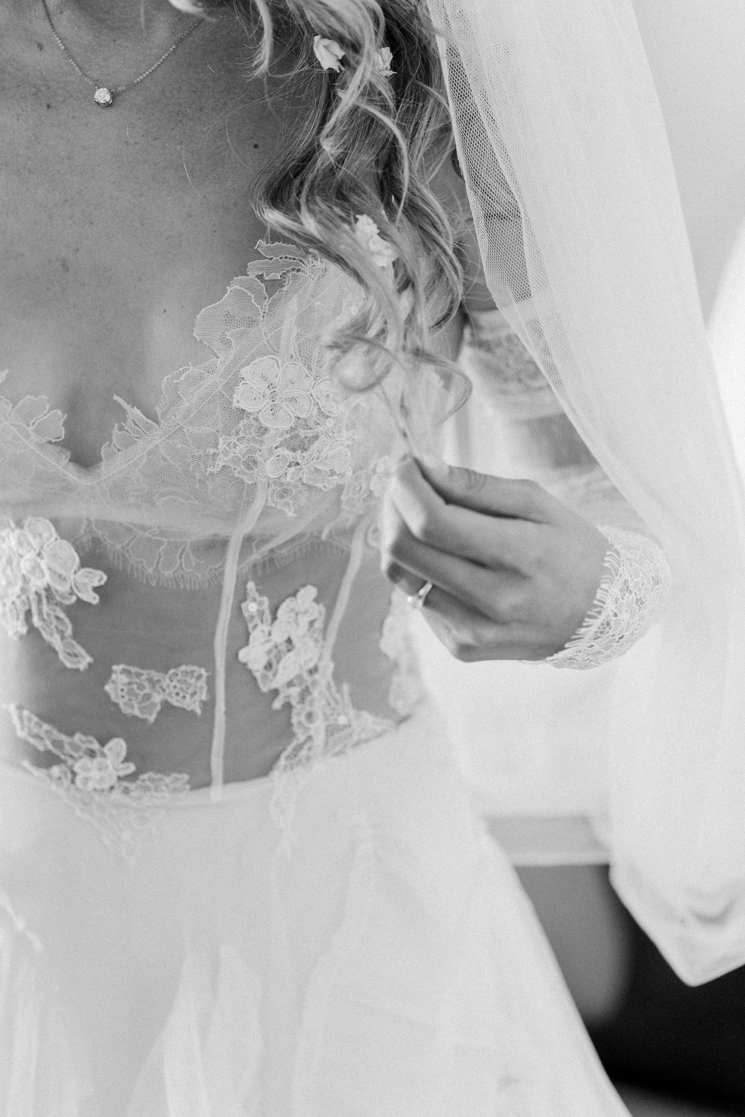 Close-up black and white detail of delicate lace wedding dress bodice with sheer fabric and intricate floral patterns.
