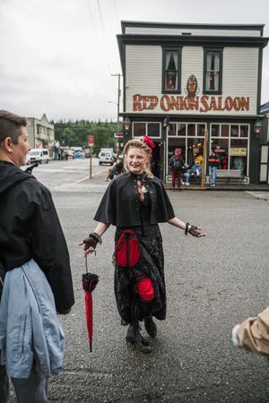 Woman in Victorian gothic costume holds red umbrella outside Red Onion Saloon in Skagway Alaska.
