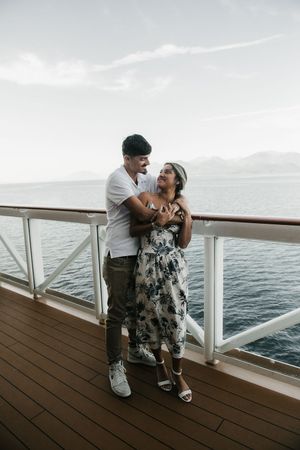 A couple embraces and smiles on a cruise ship deck with ocean views behind them.