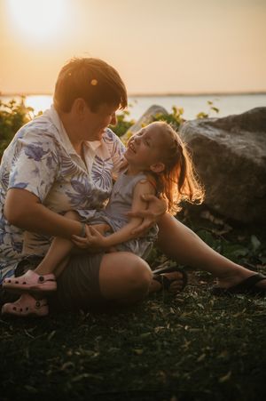 Parent and child share a tender moment while sitting outdoors during golden hour sunset.
