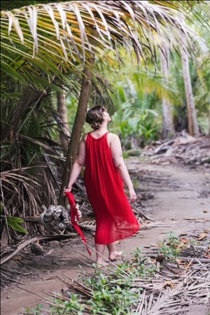 A figure in a flowing red dress explores a tropical path lined with palm trees and foliage.