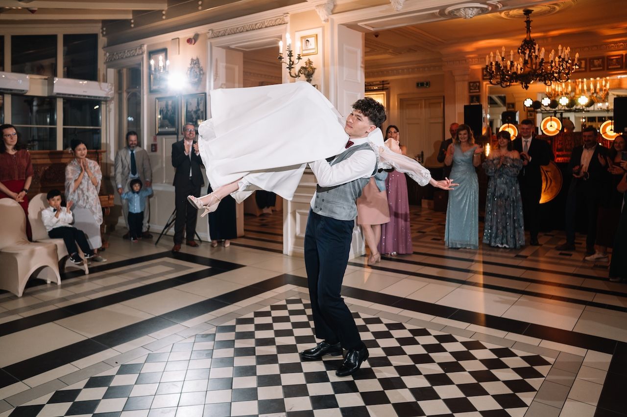 A performer twirls a white cloth on a black and white checkered dance floor at an elegant wedding reception.