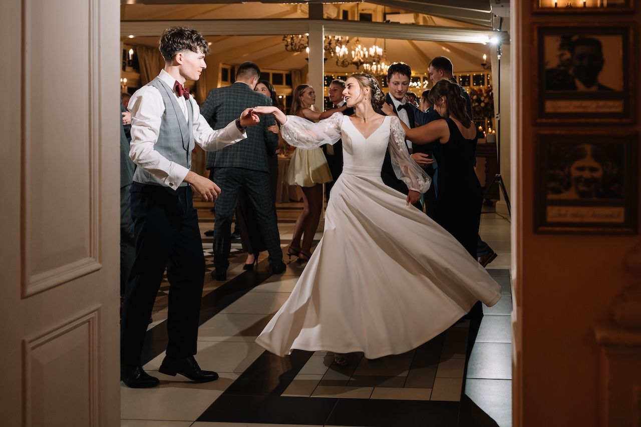 Bride and groom dancing joyfully at wedding reception, bride's white gown twirling, guests celebrating in elegant ballroom.